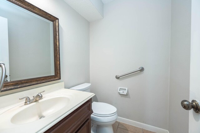 half bathroom featuring tile patterned flooring, baseboards, vanity, and toilet