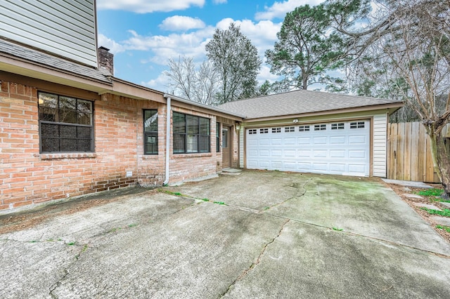 exterior space featuring an attached garage, fence, concrete driveway, and brick siding