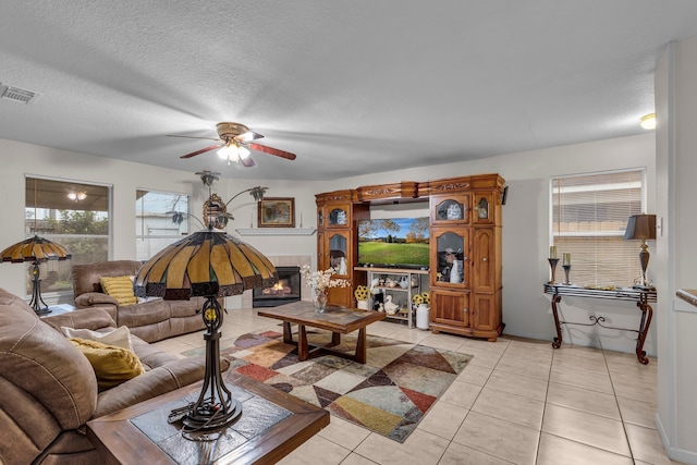 living area with visible vents, a tiled fireplace, ceiling fan, a textured ceiling, and light tile patterned flooring