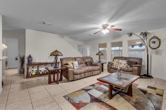 living area featuring light tile patterned floors, a ceiling fan, visible vents, and a textured ceiling