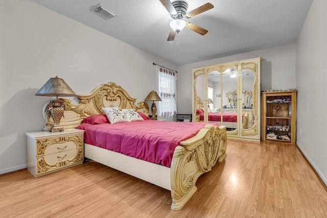 bedroom with a ceiling fan, visible vents, baseboards, and wood finished floors