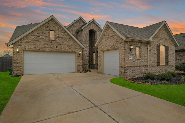 french country style house featuring brick siding, driveway, a garage, and roof with shingles