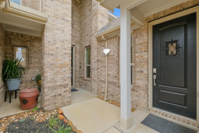 doorway to property with brick siding, covered porch, and roof with shingles