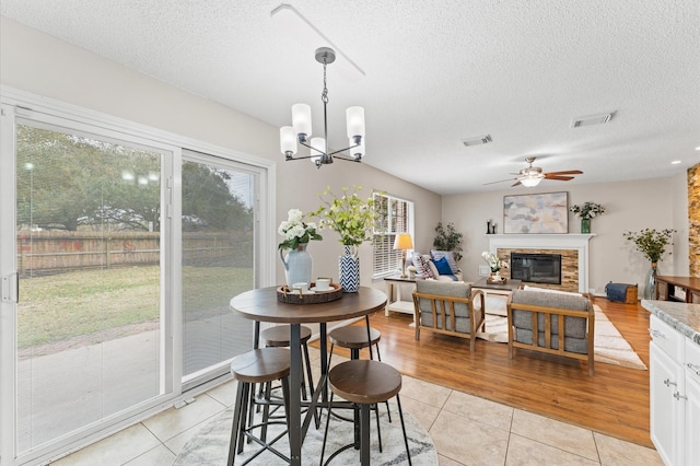 dining room with visible vents, a ceiling fan, a glass covered fireplace, and light tile patterned flooring