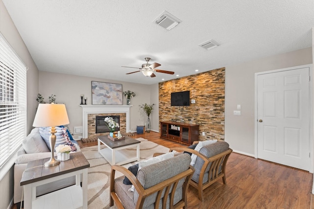 living area featuring a glass covered fireplace, wood finished floors, visible vents, and a textured ceiling