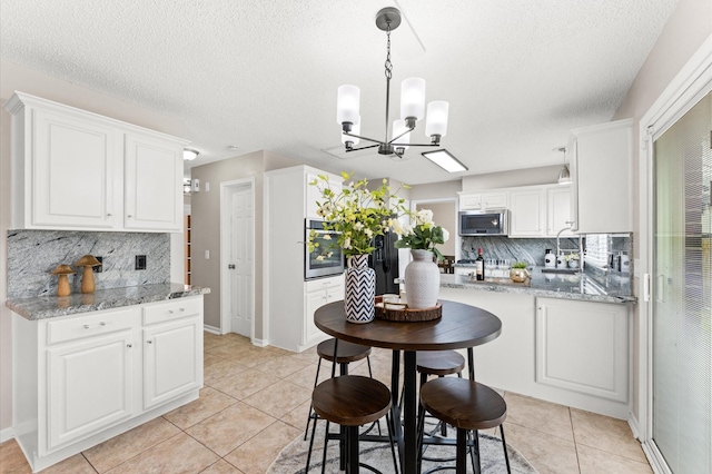 kitchen with light tile patterned flooring, stainless steel appliances, decorative backsplash, white cabinets, and pendant lighting