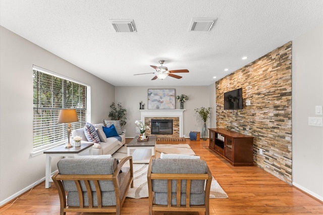 living area featuring visible vents, a ceiling fan, light wood-style floors, and a glass covered fireplace