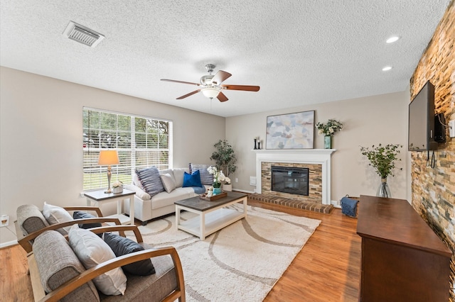 living room with ceiling fan, visible vents, a glass covered fireplace, and light wood-style flooring