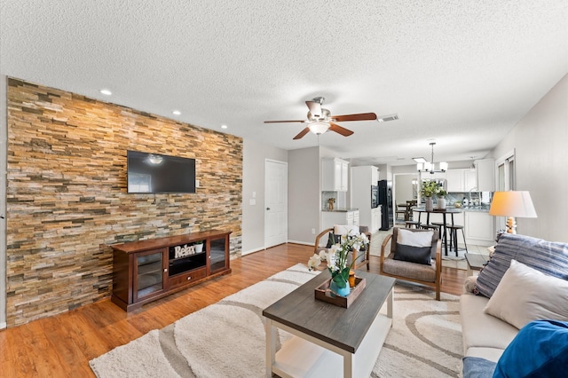 living area featuring visible vents, ceiling fan with notable chandelier, a textured ceiling, and light wood finished floors