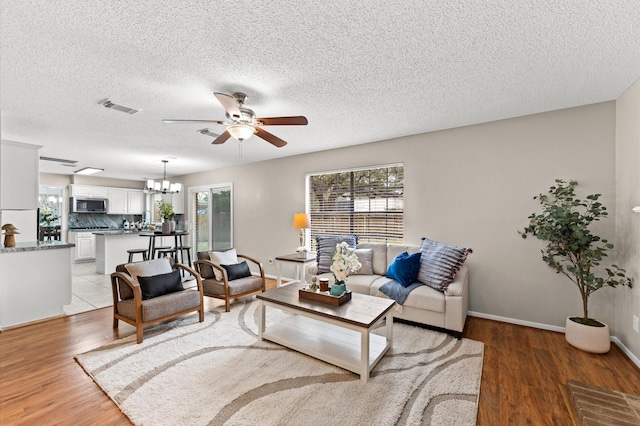 living room featuring visible vents, baseboards, light wood-type flooring, ceiling fan with notable chandelier, and a textured ceiling