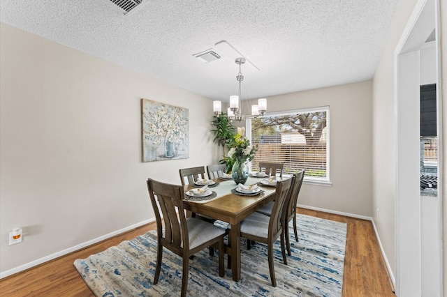 dining space featuring a chandelier, a textured ceiling, visible vents, and wood finished floors