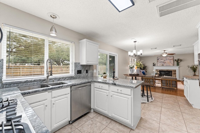 kitchen featuring visible vents, a peninsula, a fireplace, a sink, and dishwasher