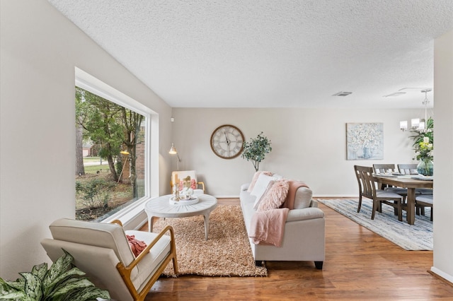 living room featuring visible vents, a notable chandelier, a textured ceiling, wood finished floors, and baseboards