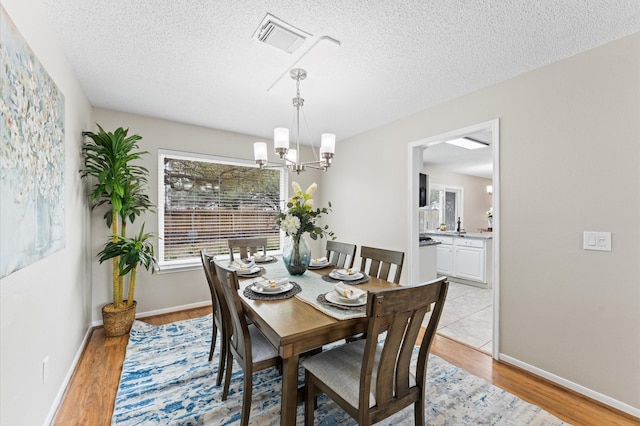 dining space featuring visible vents, a textured ceiling, light wood-style flooring, and a chandelier