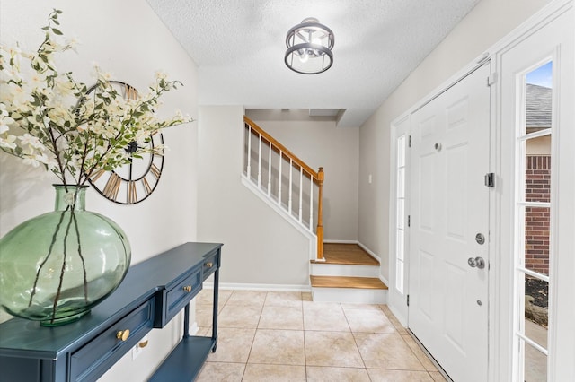 foyer featuring stairway, light tile patterned floors, baseboards, and a textured ceiling