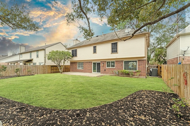 back of property with brick siding, central air condition unit, a fenced backyard, a yard, and a patio area