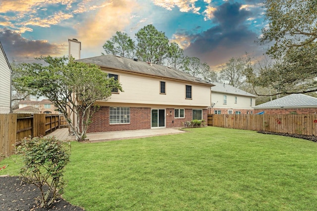 back of property at dusk with brick siding, a lawn, a chimney, a fenced backyard, and a patio