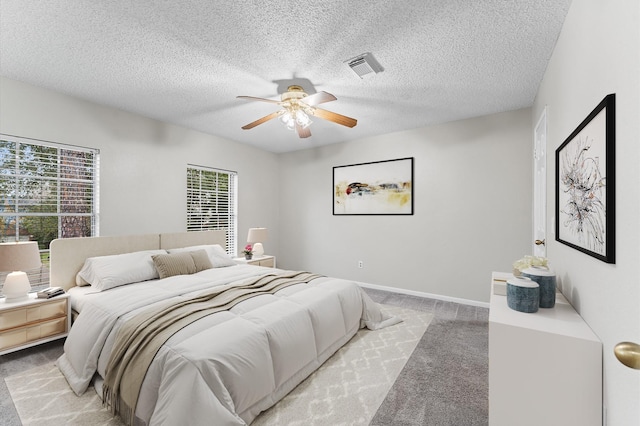 bedroom with visible vents, light carpet, a textured ceiling, and baseboards