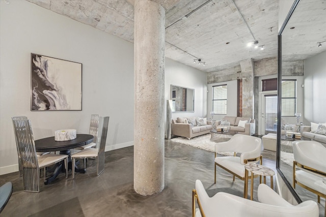 living area with rail lighting, finished concrete flooring, baseboards, and decorative columns