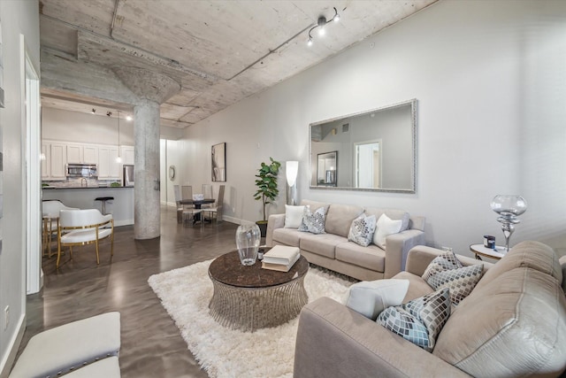 living area featuring rail lighting, decorative columns, and baseboards