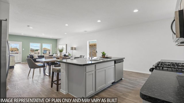 kitchen with appliances with stainless steel finishes, wood finished floors, a center island, a sink, and recessed lighting