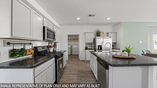 kitchen with stainless steel appliances, a sink, visible vents, dark countertops, and washing machine and clothes dryer