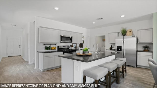 kitchen featuring light wood finished floors, appliances with stainless steel finishes, a breakfast bar, and a sink