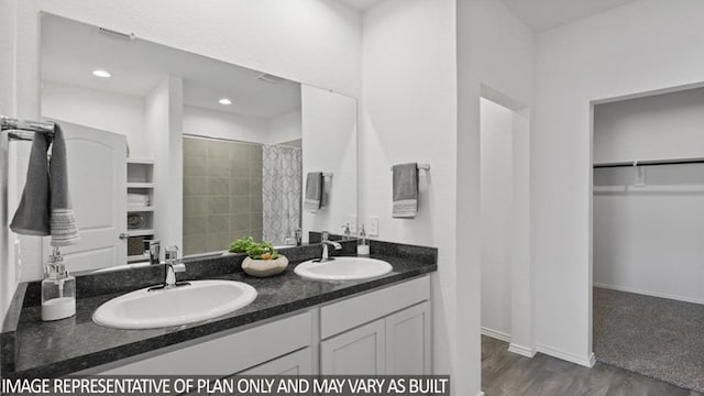 bathroom featuring double vanity, a walk in closet, a sink, and wood finished floors