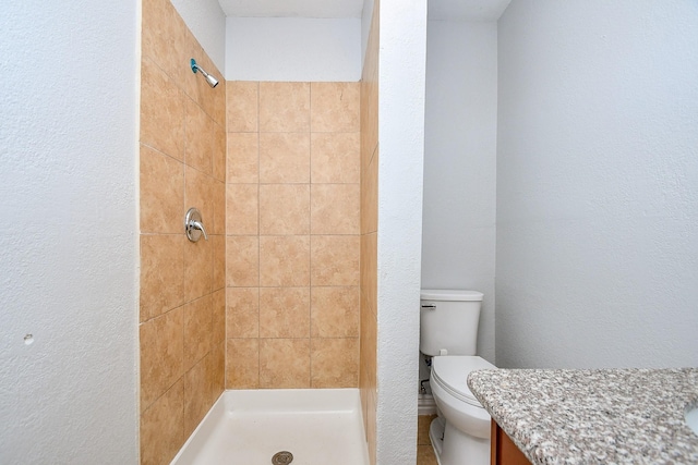 full bath with toilet, a stall shower, vanity, and a textured wall