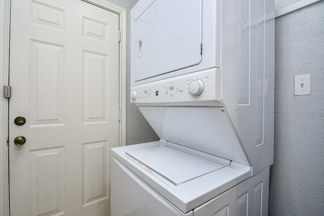 clothes washing area featuring laundry area, a textured wall, and stacked washer and clothes dryer