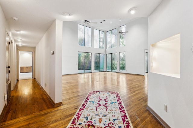 interior space featuring ceiling fan, a towering ceiling, baseboards, and wood finished floors