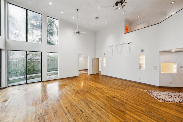 unfurnished living room featuring a ceiling fan, a healthy amount of sunlight, a high ceiling, and wood finished floors