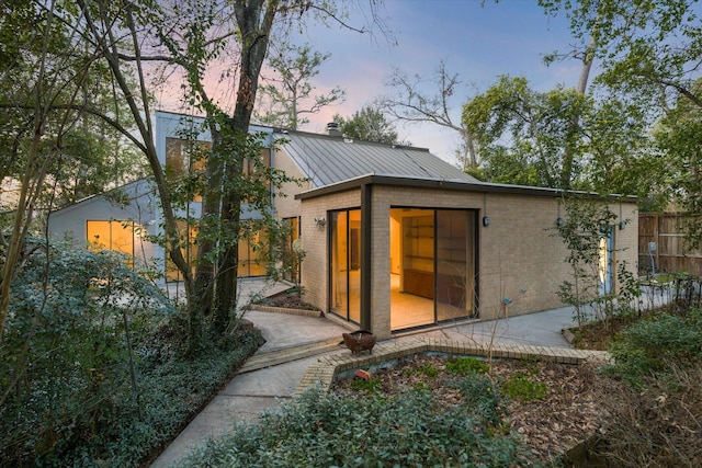 rear view of property featuring metal roof, a standing seam roof, fence, a patio area, and brick siding