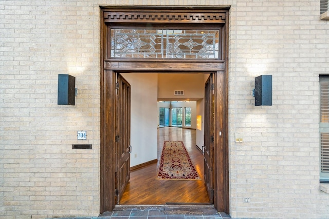 view of exterior entry featuring visible vents, brick siding, and a balcony