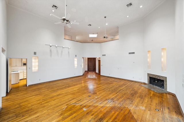 unfurnished living room with a ceiling fan, light wood-type flooring, visible vents, and a fireplace with flush hearth