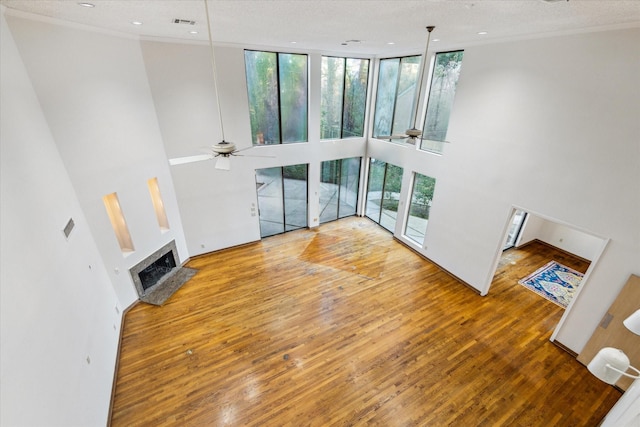 unfurnished living room with ceiling fan, a fireplace with raised hearth, a high ceiling, visible vents, and hardwood / wood-style floors