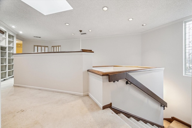 interior space featuring light carpet, a skylight, baseboards, and a textured ceiling