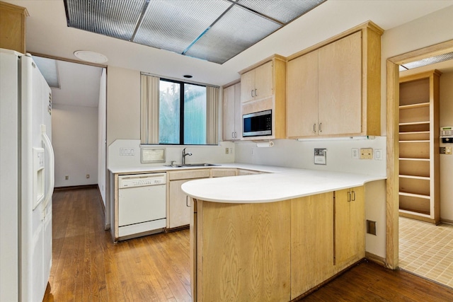 kitchen featuring a peninsula, white appliances, a sink, light countertops, and light brown cabinetry