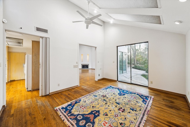 unfurnished room with ceiling fan, a fireplace, wood finished floors, and visible vents