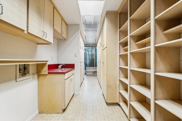 interior space with light floors, baseboards, a sink, and light brown cabinetry