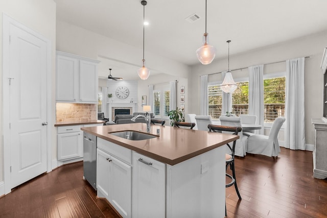 kitchen featuring tasteful backsplash, a sink, a brick fireplace, dark wood-style floors, and stainless steel dishwasher