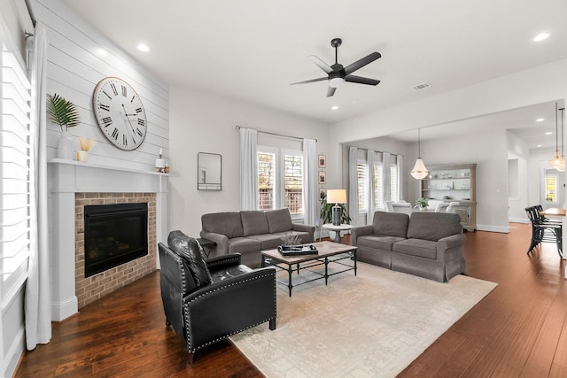 living room featuring dark wood-type flooring, a brick fireplace, recessed lighting, and visible vents