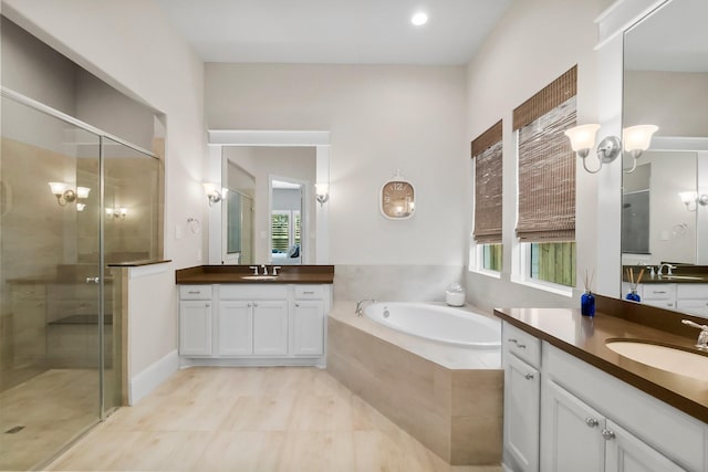 bathroom featuring a sink, two vanities, a stall shower, and a bath