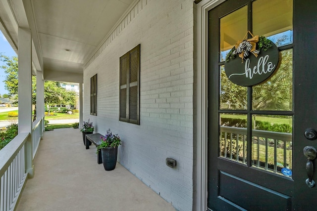 doorway to property featuring a porch and brick siding