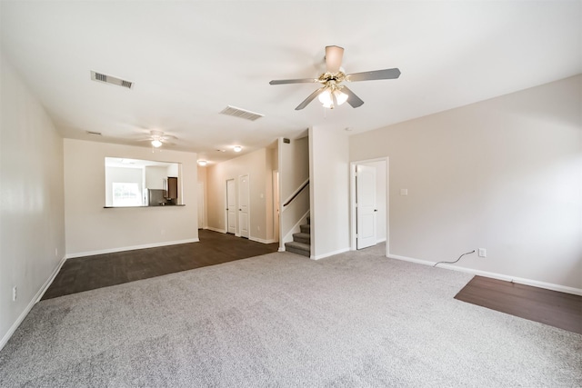 spare room featuring stairs, dark colored carpet, visible vents, and a ceiling fan