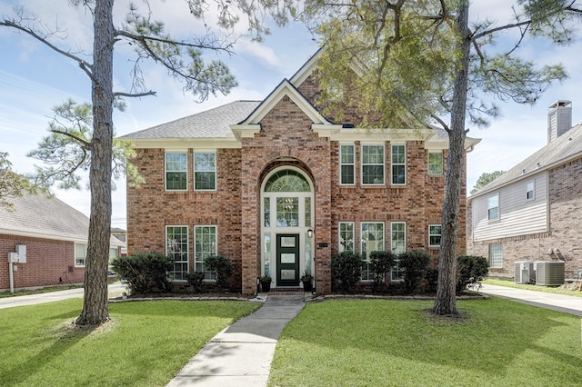 view of front facade with a front yard, brick siding, and central air condition unit