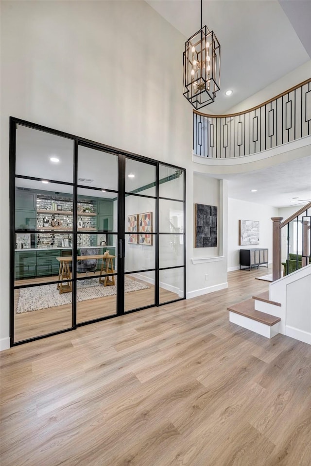 interior space featuring stairway, a towering ceiling, wood finished floors, a chandelier, and baseboards