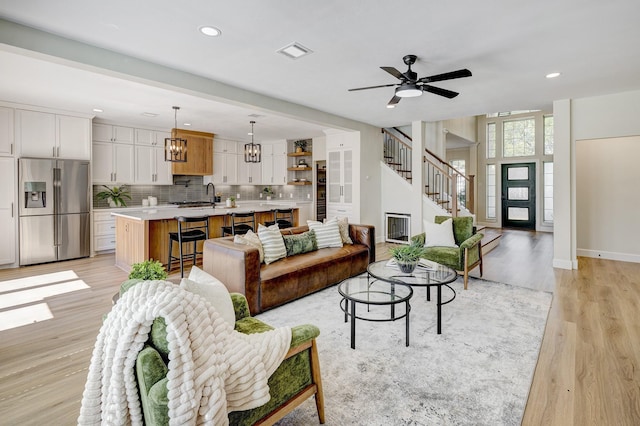 living area with recessed lighting, visible vents, light wood-type flooring, baseboards, and stairs