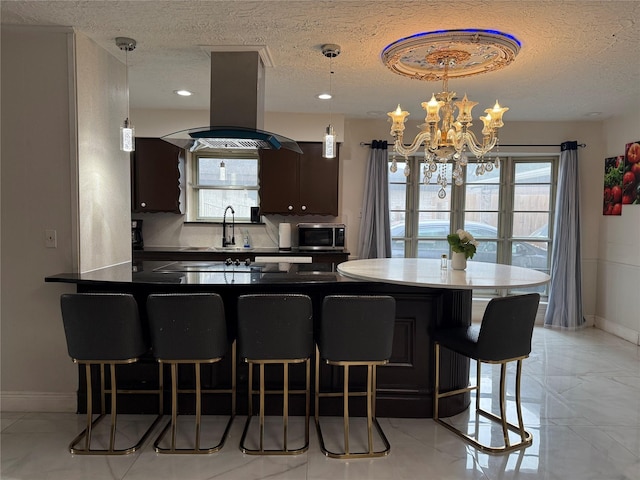 kitchen featuring dark countertops, stainless steel microwave, a textured ceiling, island range hood, and baseboards