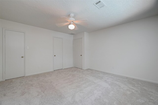 unfurnished bedroom featuring visible vents, light carpet, ceiling fan, a textured ceiling, and baseboards